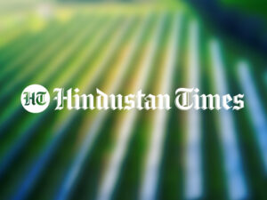 The Hindustan Times logo over a blurred photo of a solar park in a green field