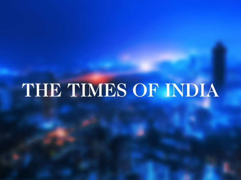 The Time os India logo over a blurred photo of a blue light india skyline